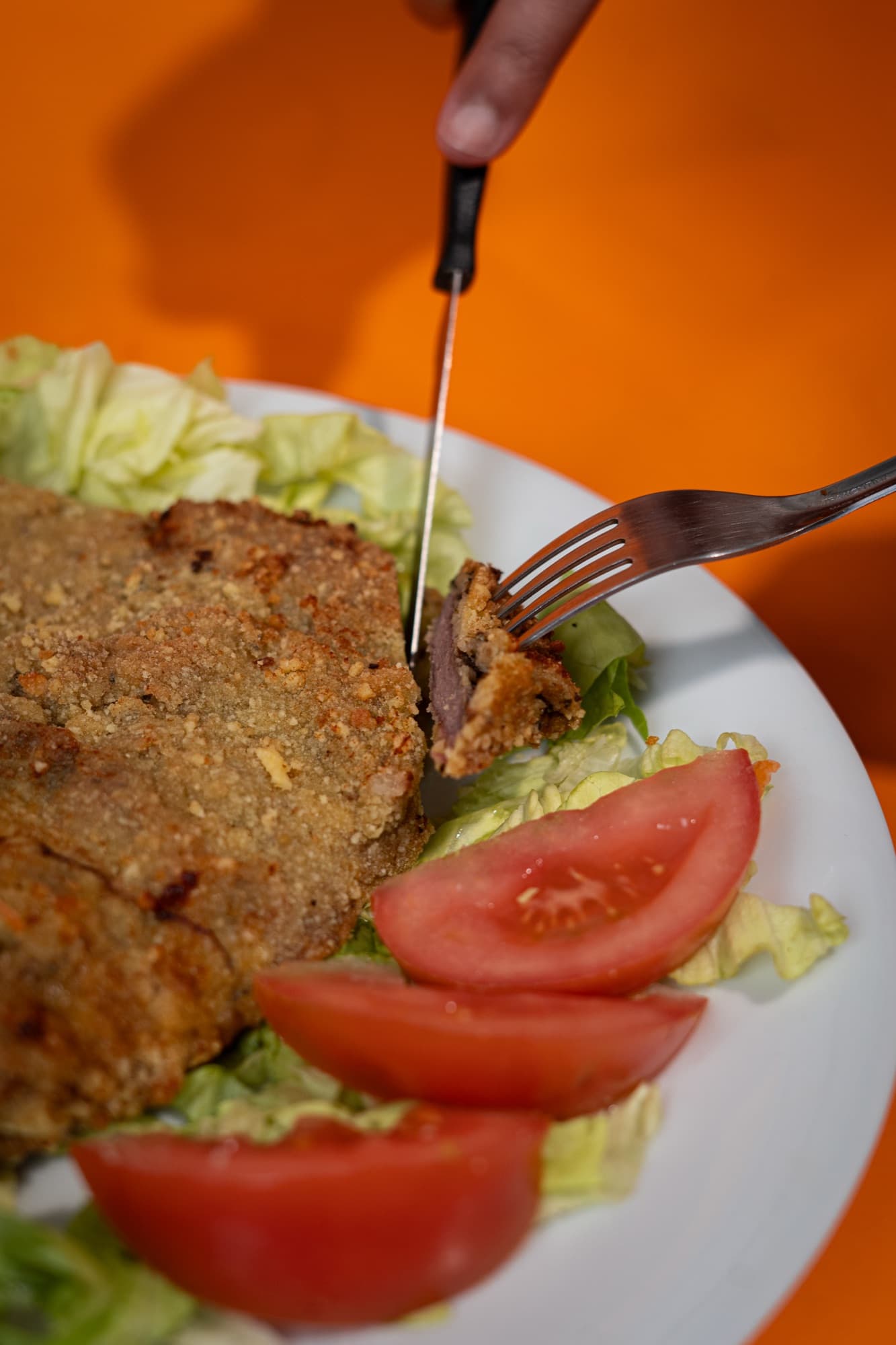 Milanesa con lechuga y tomate, cortada con cuchillo y tenedor